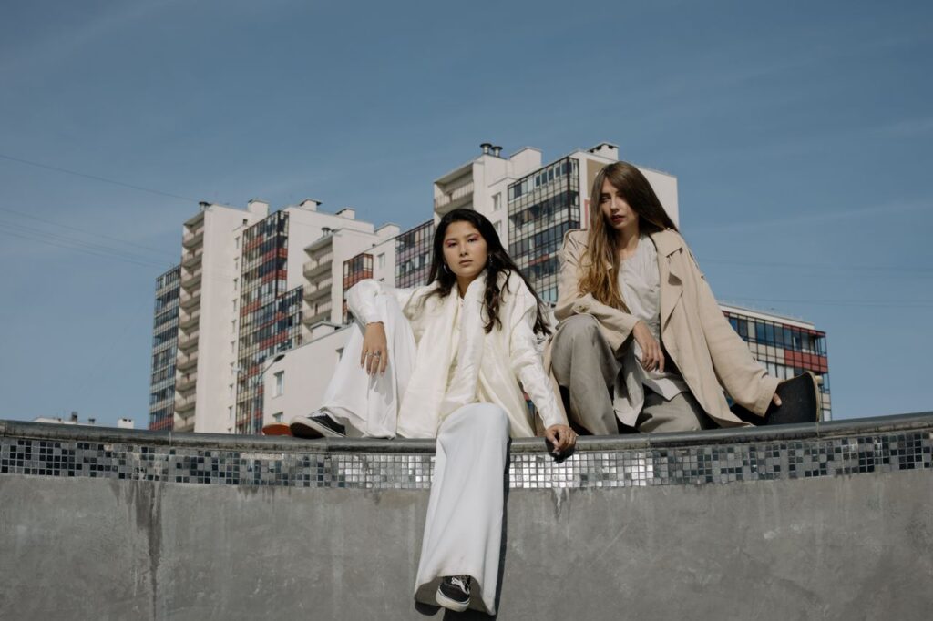 Two fashionable women sitting outdoors against a backdrop of urban buildings.